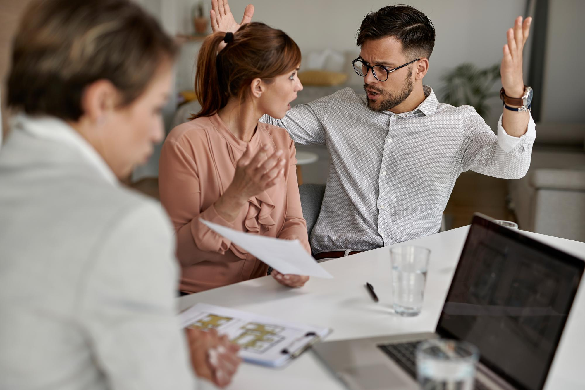 A man and woman in a heated discussion during a workplace meeting, with a colleague observing—illustrating how to deal with conflict in the workplace through active management.