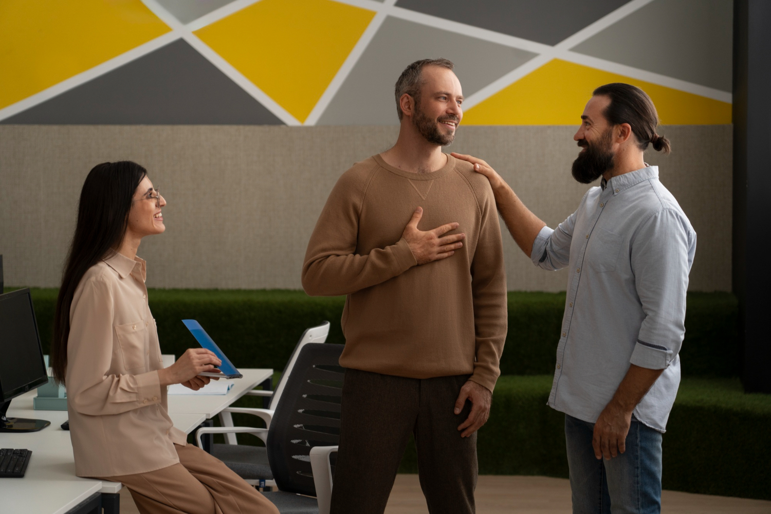 Three co-workers talking to each other, smiling, touching their shoulders and looking engaged in the conversation, which is a clear indication of how to successfully use nonverbal communication in the workplace.