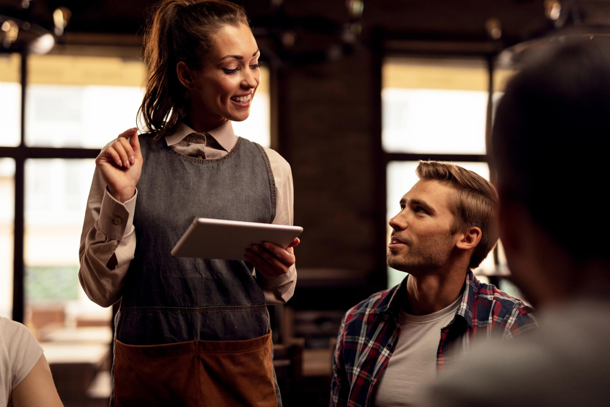 Waitress using a tablet while engaging with a customer, a real-world example of communication skills training for employees in customer-facing roles.
