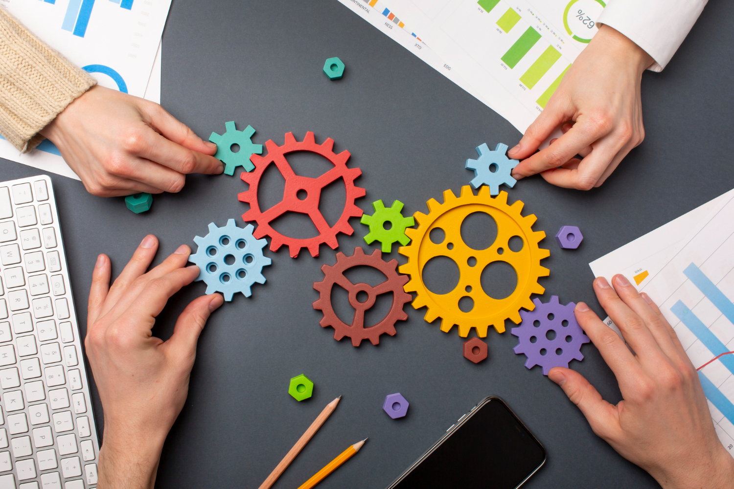 Hands putting together colored gears on the background of a corporate desk, symbolizing the effort to find strategies to boost employee productivity.