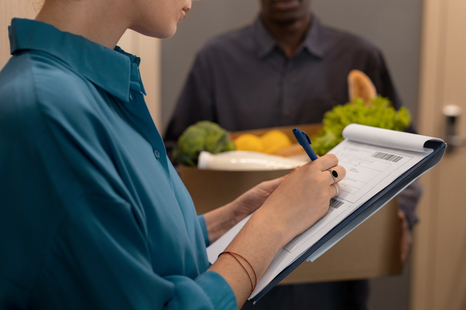 A woman completing a shift handover template with a man holding groceries in the background, signifying changing the shift in a hospitality team.
