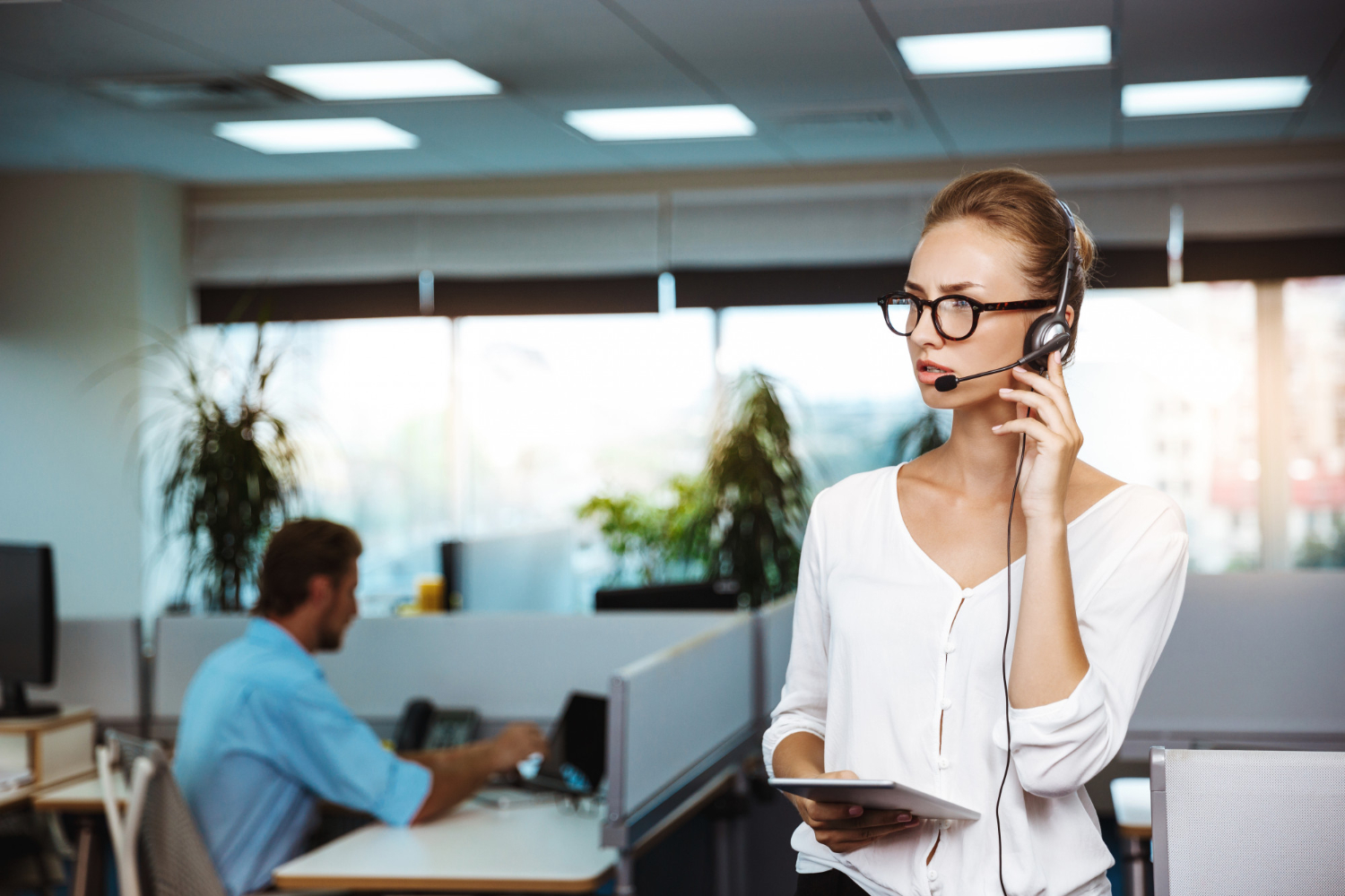 Customer service representative wearing a headset and holding a tablet in a modern office, demonstrating skills learned through telephone manner training.