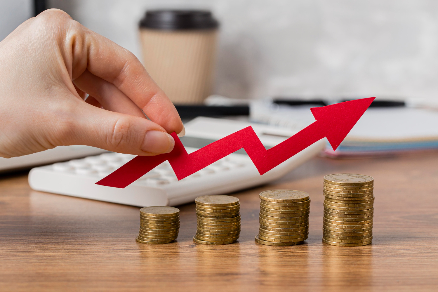 Hand holding a red upward arrow above stacks of coins, symbolizing financial growth and improved training ROI.