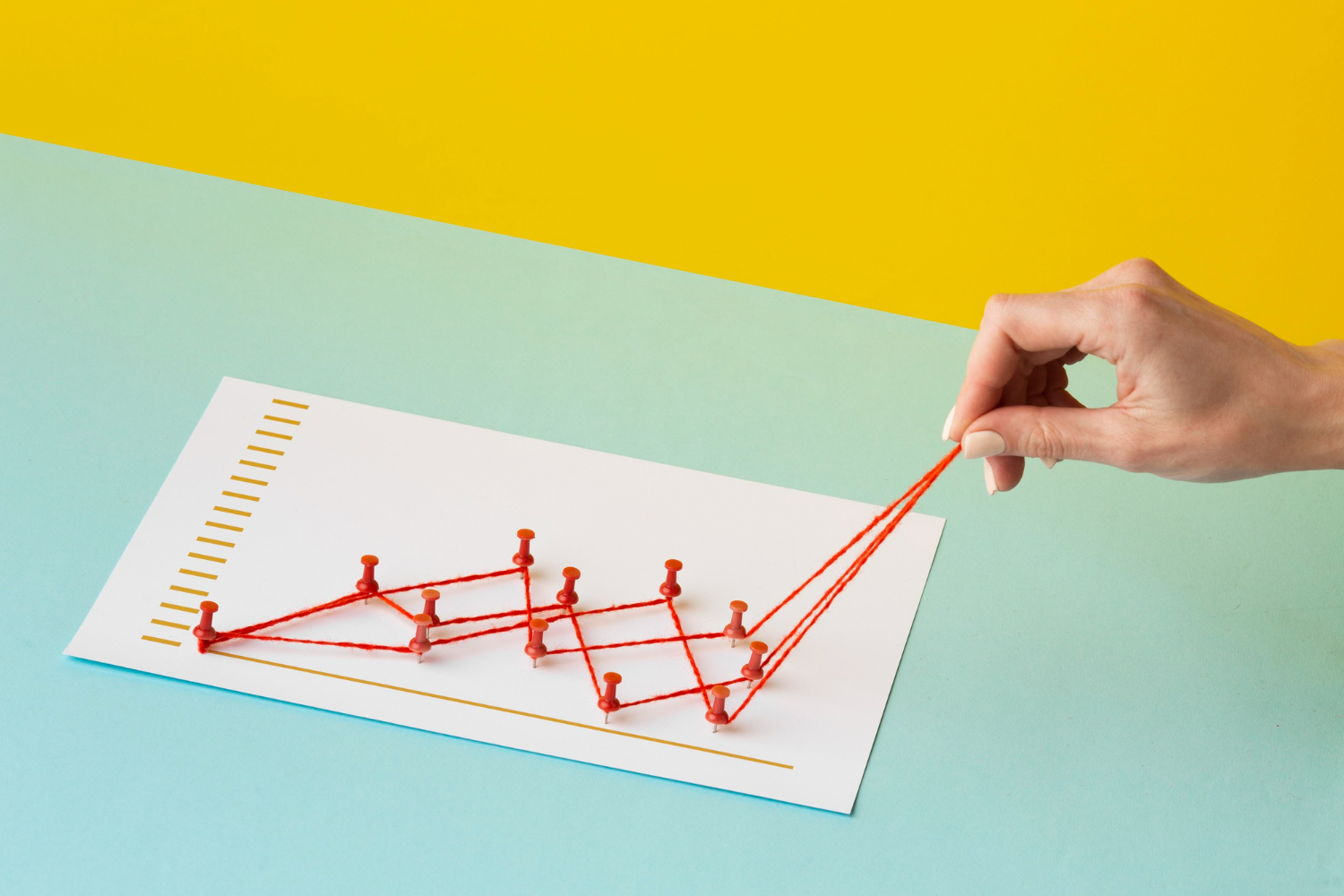 A hand pulling red thread through pins on a graph to form an upward trend, symbolizing structured progress and measurable growth in training engagement strategies.